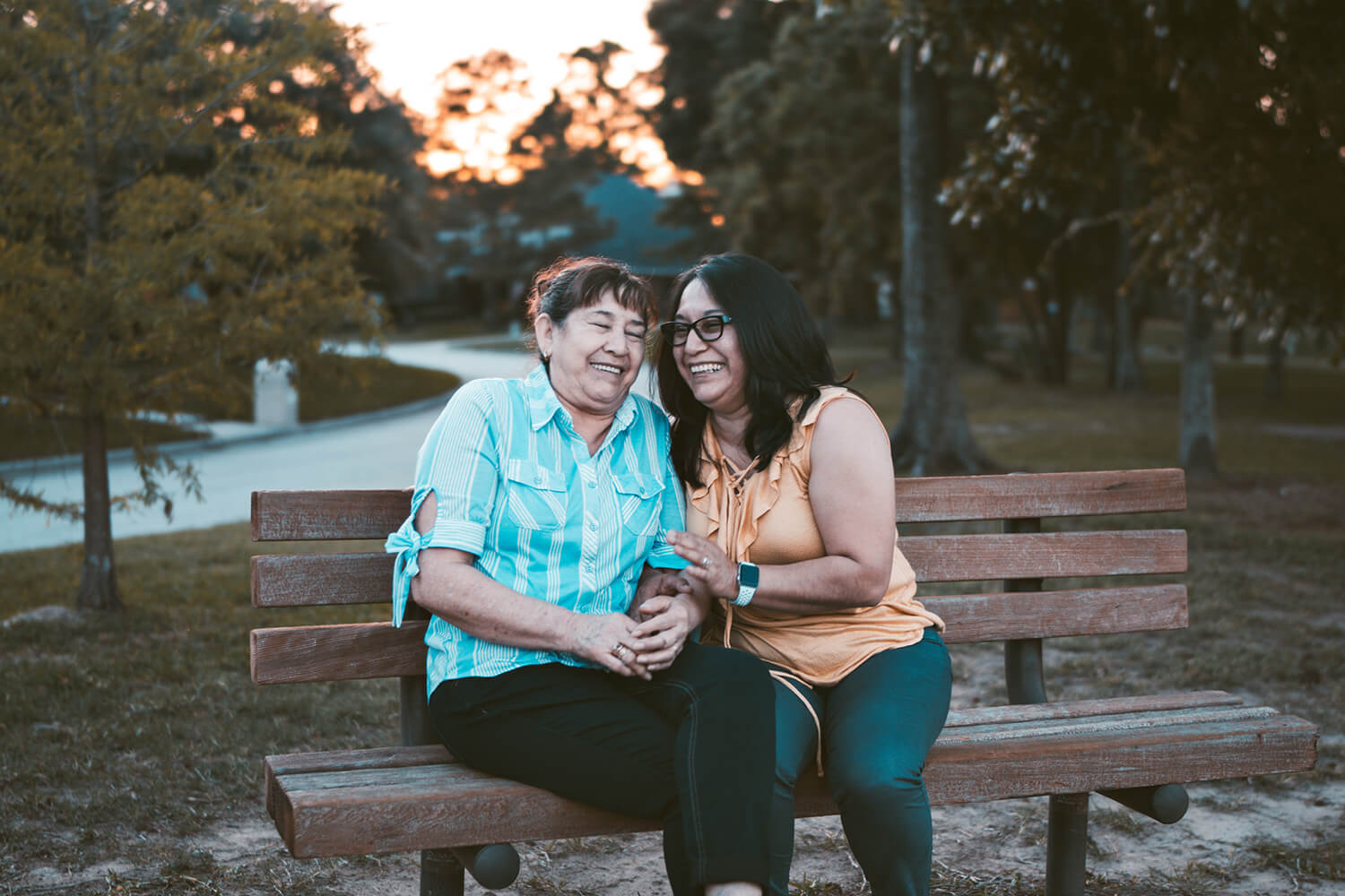 two latino women laughing on a bench in the park